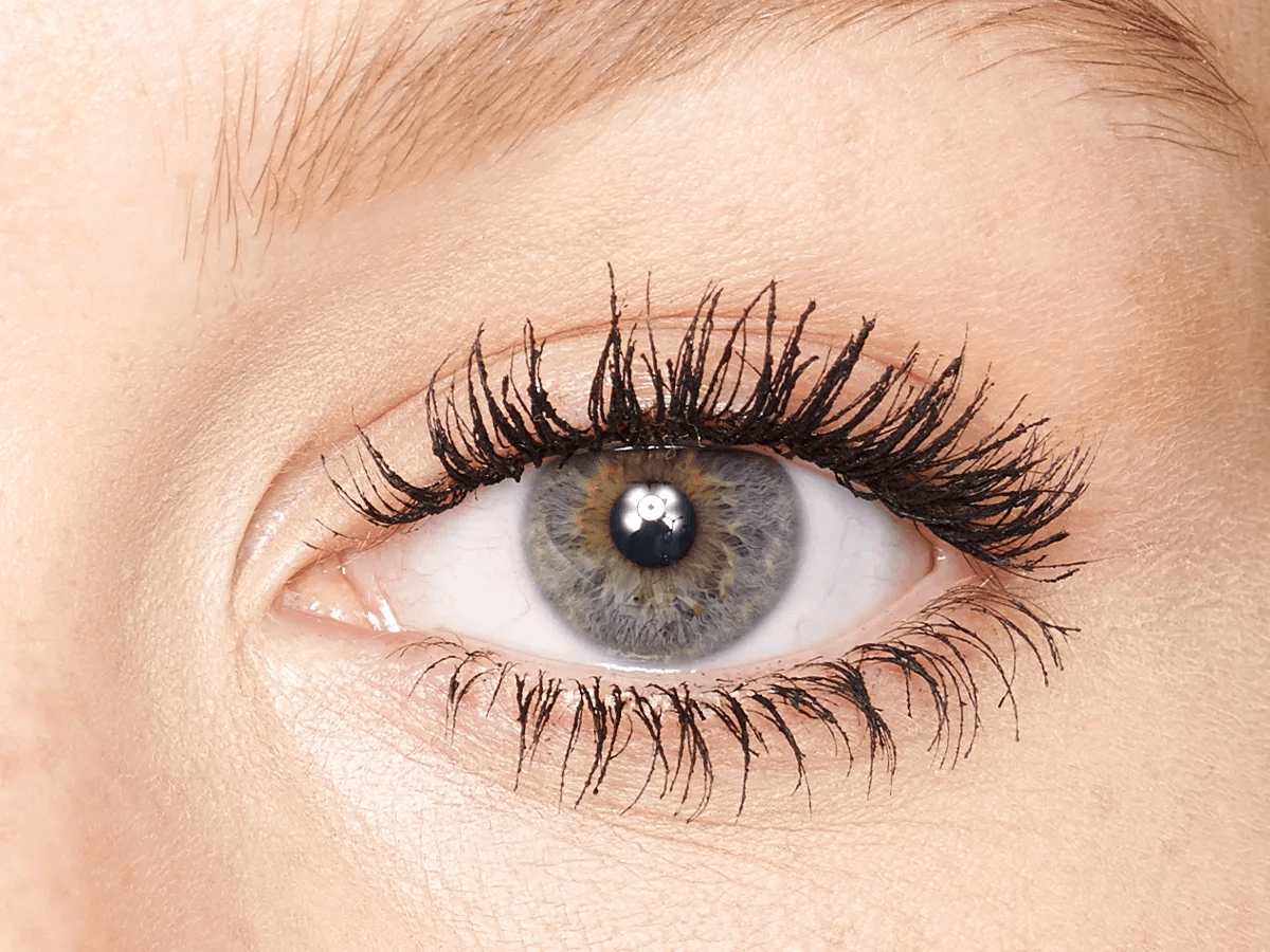 Single-eye close-up of a fair-tone model with grey eyes wearing jet-black lengthening and curling mascara. 